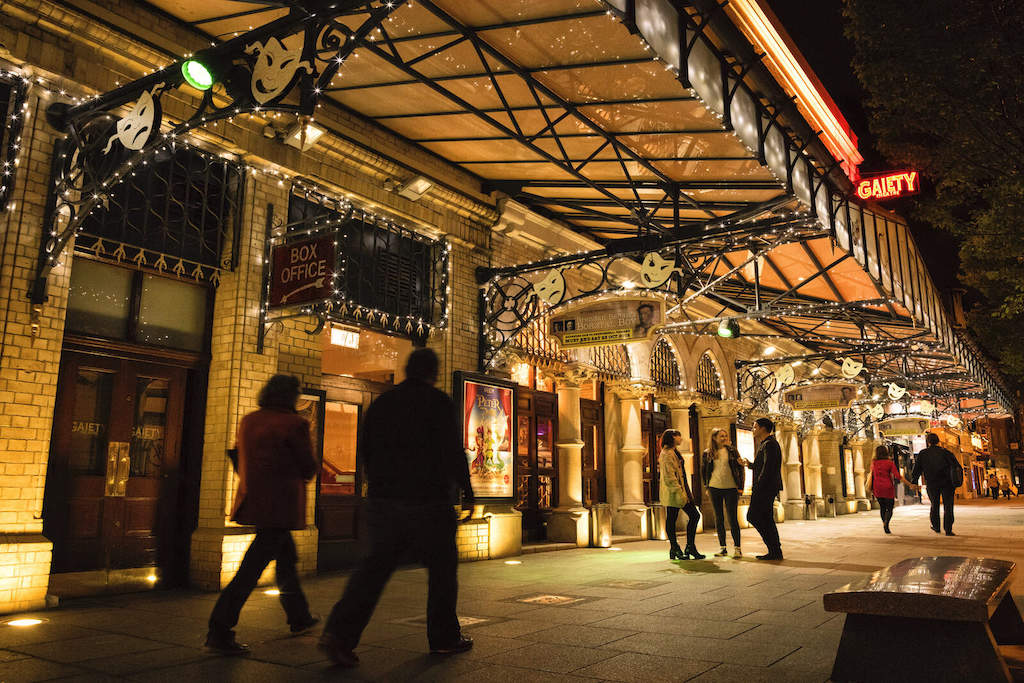 People outside the Gaiety Theatre in Dublin lit up with festive lights at night.