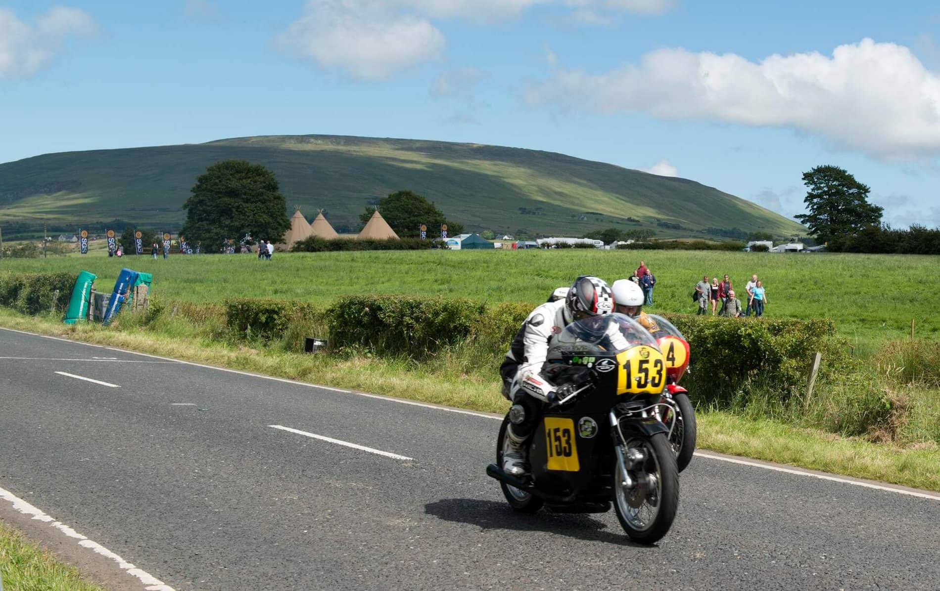Vintage-style motorcycle racer in black leathers speeding past rural fields during the Armoy Road Races in County Antrim.