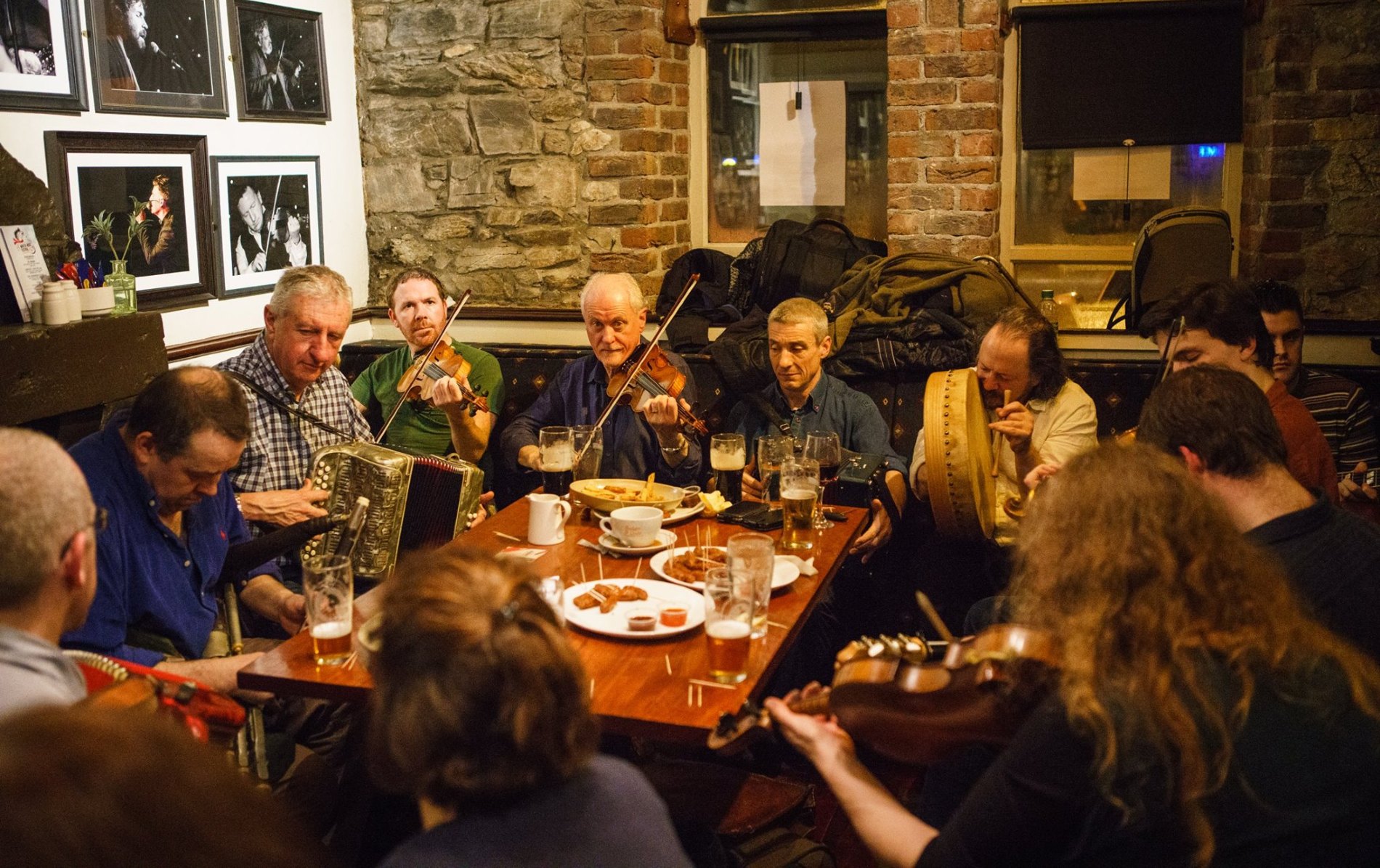 Trad musicians play fiddle, bodhrán and accordion around a table at The White House, Limerick.