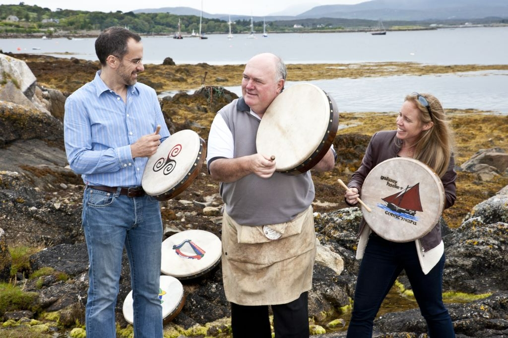 People enjoying a traditional bodhrán drumming session outdoors by the shore in Connemara, County Galway.