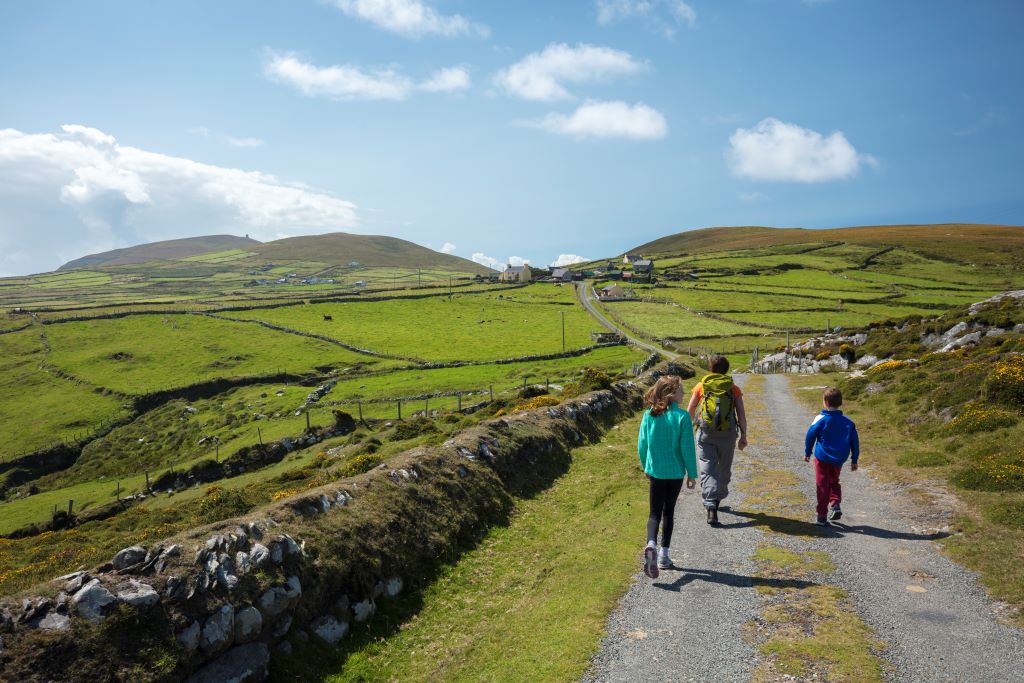 Family walking along a country lane through rolling green fields on Dursey Island in County Cork.