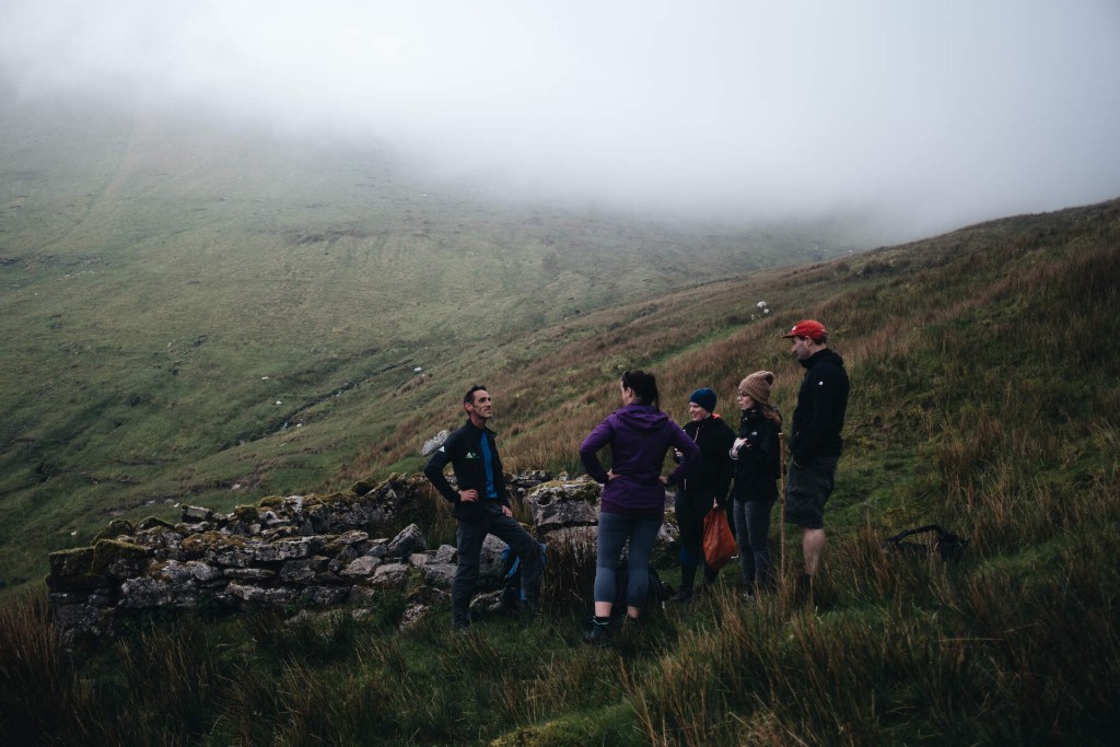 Group of hikers resting by a stone wall on misty slopes beneath Ben Bulben in County Sligo.