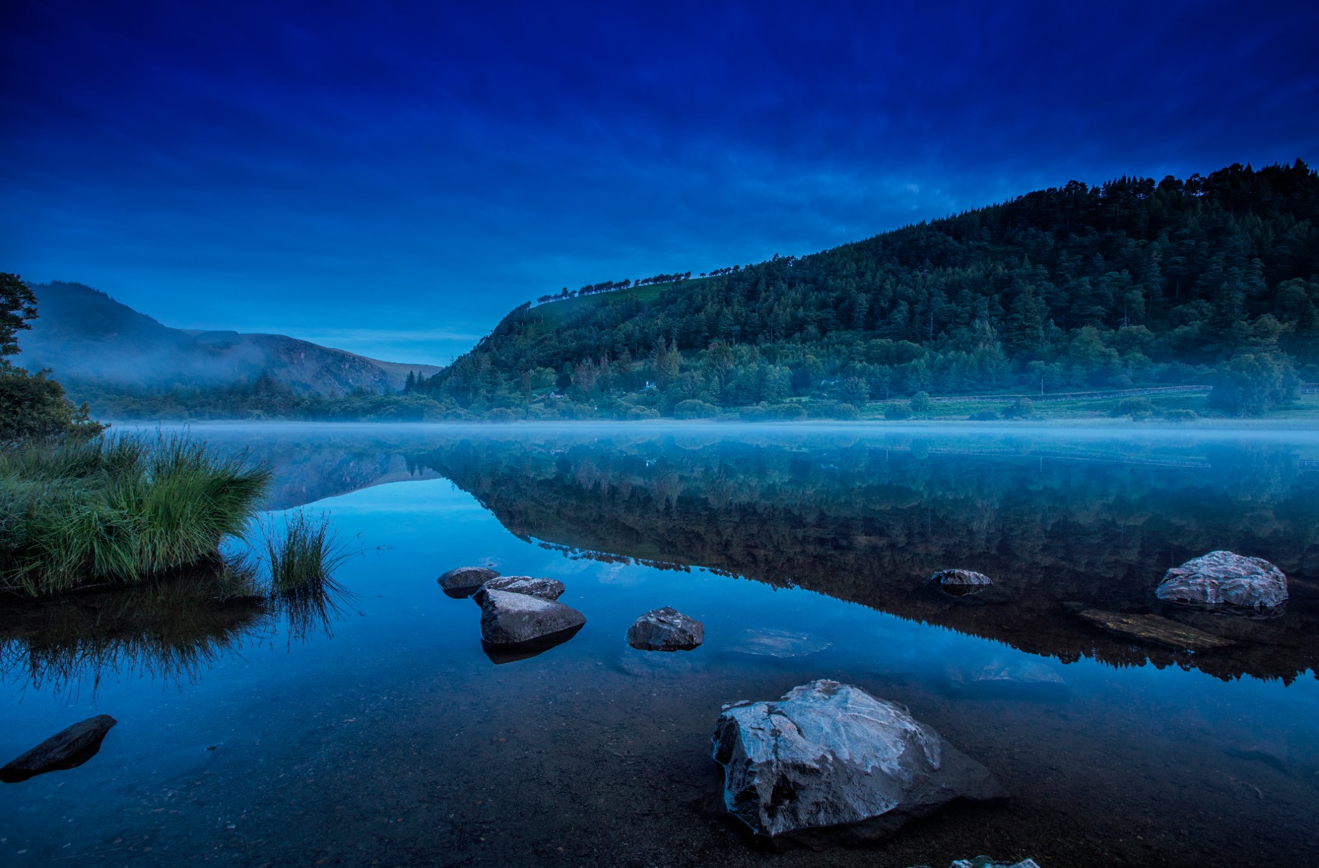 Misty morning reflection of forested hills on Upper Lake, Glendalough, County Wicklow.