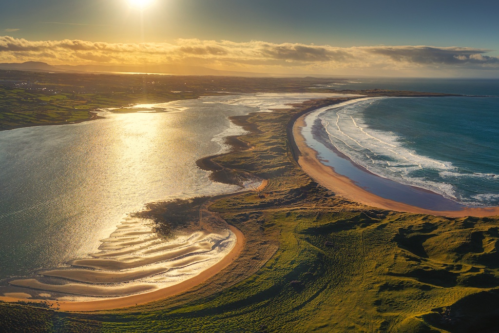 Aerial view of Streedagh Beach’s sandy curve and rolling waves under the evening sun.