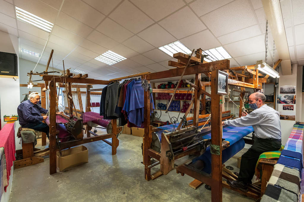 Two craftsmen weave at wooden looms inside Triona Donegal Tweed Visitor Centre in Ardara, showcasing traditional textile work.