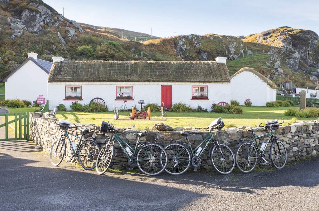 Bicycles lean against a stone wall in front of the traditional thatched cottages of Glencolmcille Folk Village, Donegal.