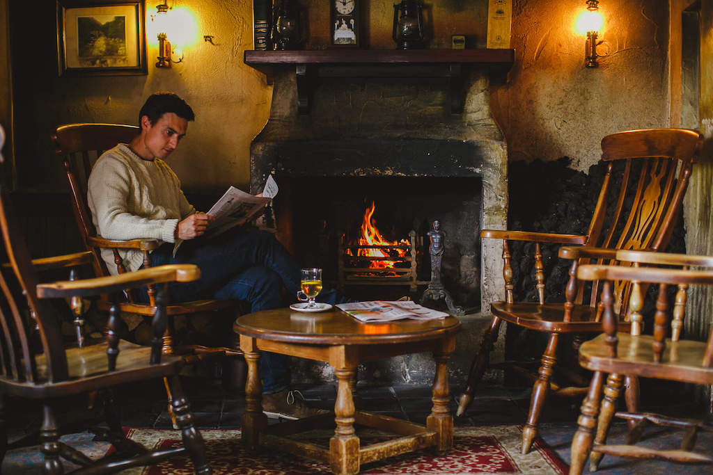 Man reading by a glowing fire with a drink in The Bushmills Inn, County Antrim.