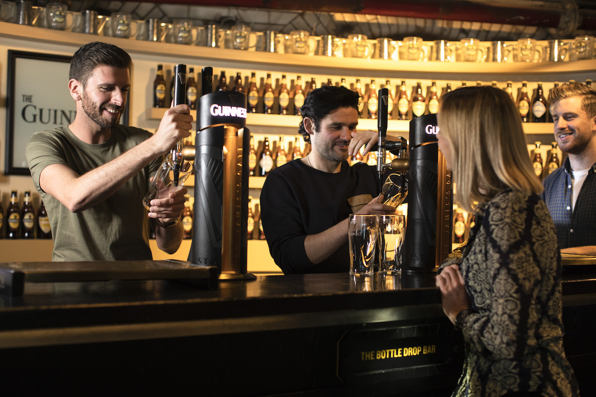 Bartenders pour pints of Guinness for visitors at The Bottle Drop Bar in Dublin.