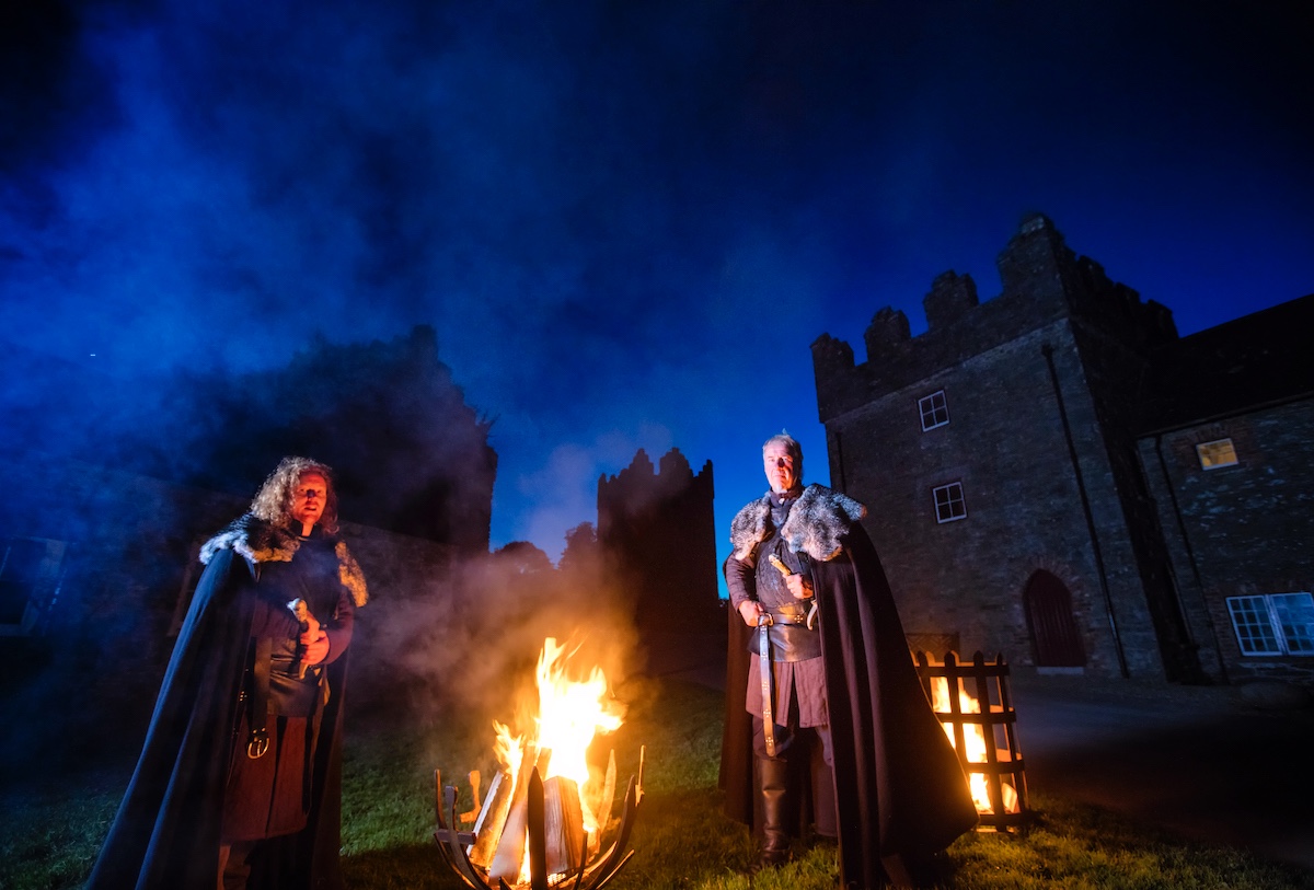 Two costumed actors stand by a fire at night on the Winterfell Tours in County Down.