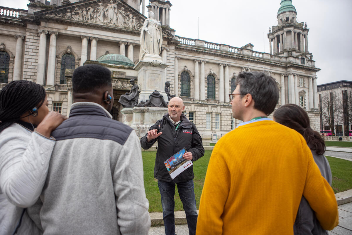 Guide leading a walking tour outside Belfast City Hall in Belfast city centre.