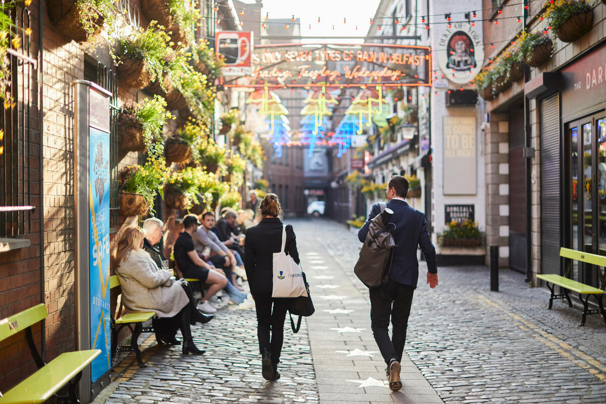 People walking through Commercial Court in Belfast's Cathedral Quarter beneath colourful overhead lights.