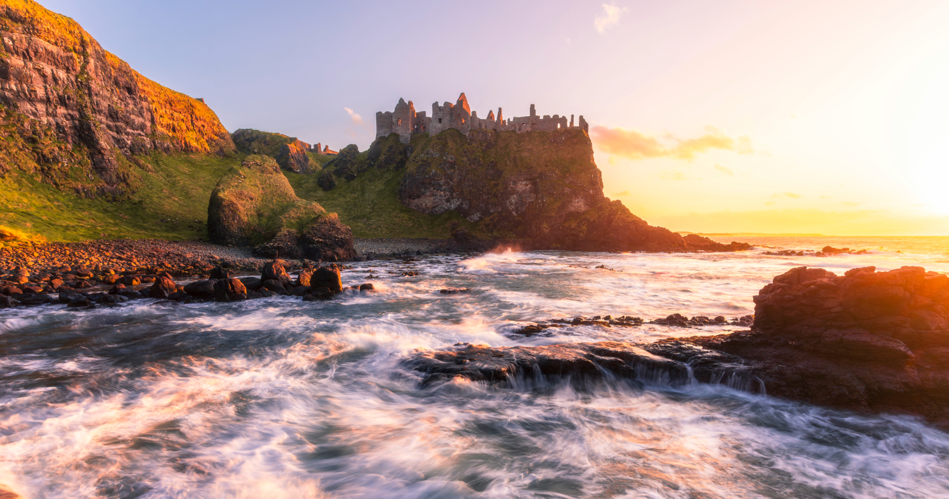 Dunluce Castle above crashing waves on the Causeway Coast at sunset, County Antrim.