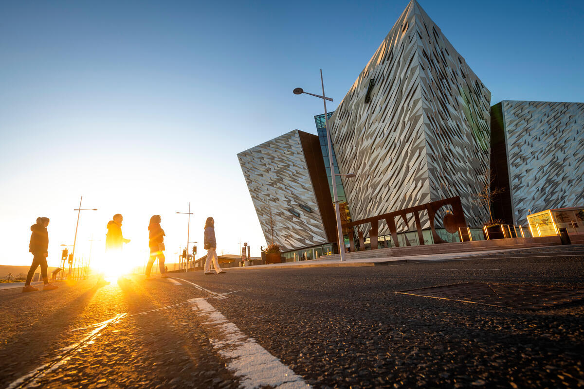 People walking past Titanic Belfast at sunrise in the Titanic Quarter.