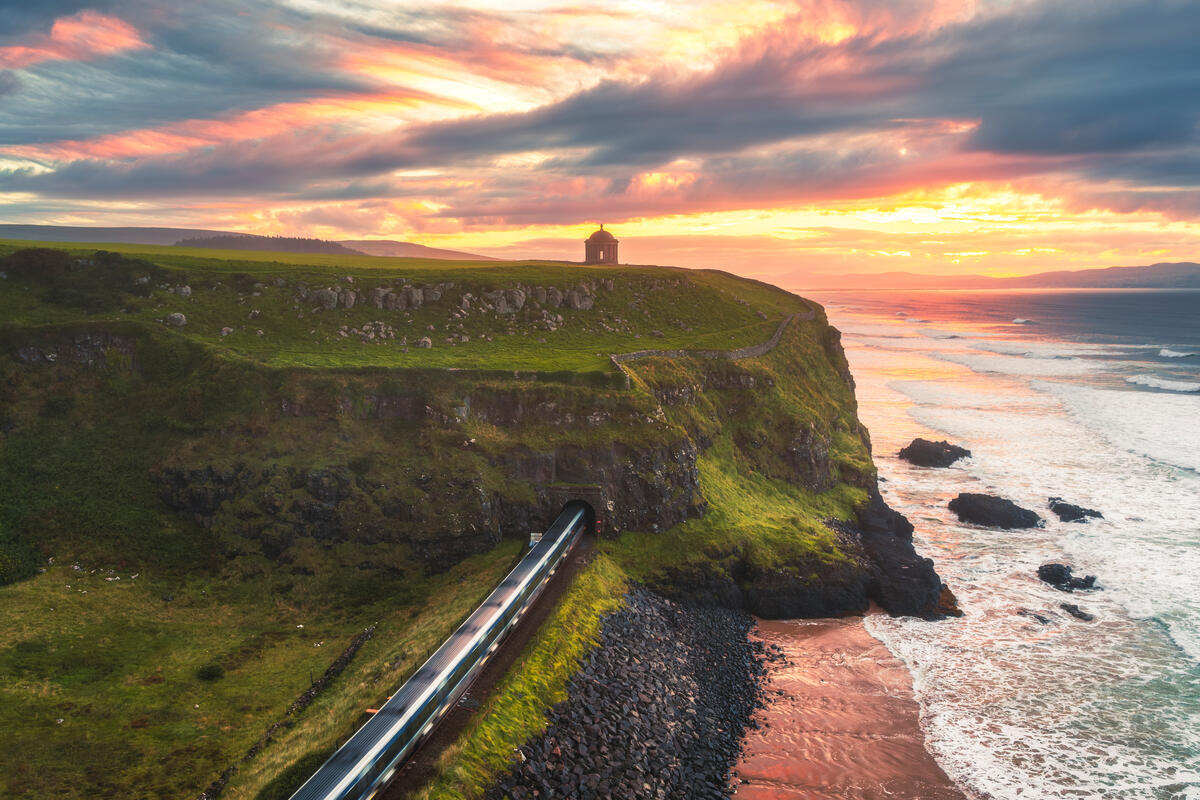 Train emerging beneath Mussenden Temple beside Downhill Strand at sunset, County Londonderry.