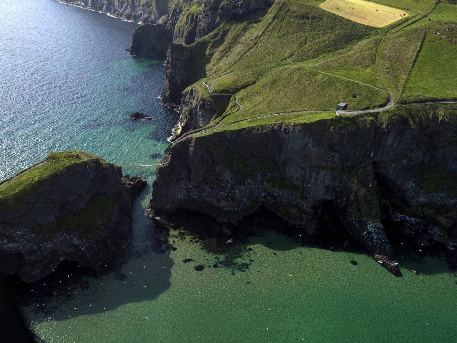 Aerial view of Carrick-a-Rede Rope Bridge stretching across cliffs above turquoise waters in County Antrim.