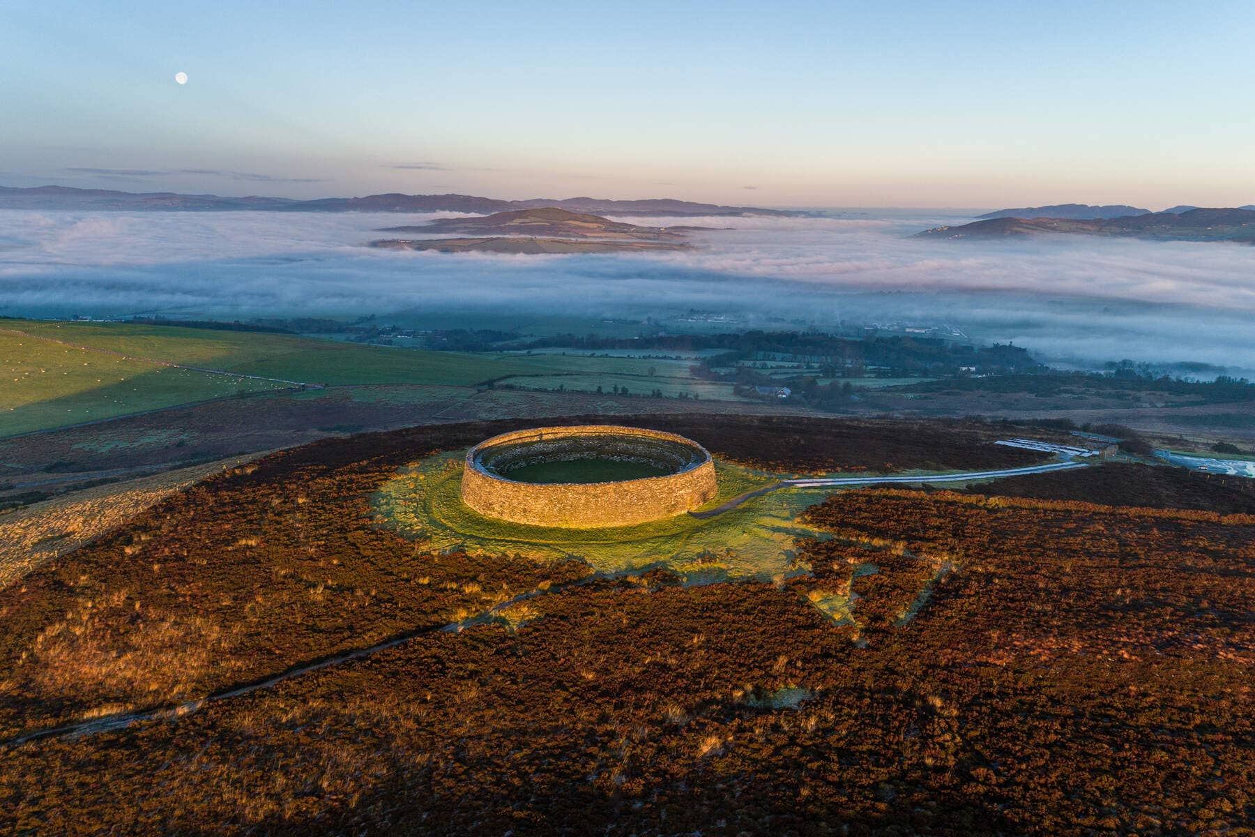 Aerial view of An Grianán of Aileach ring fort at sunrise, surrounded by misty hills in County Donegal.