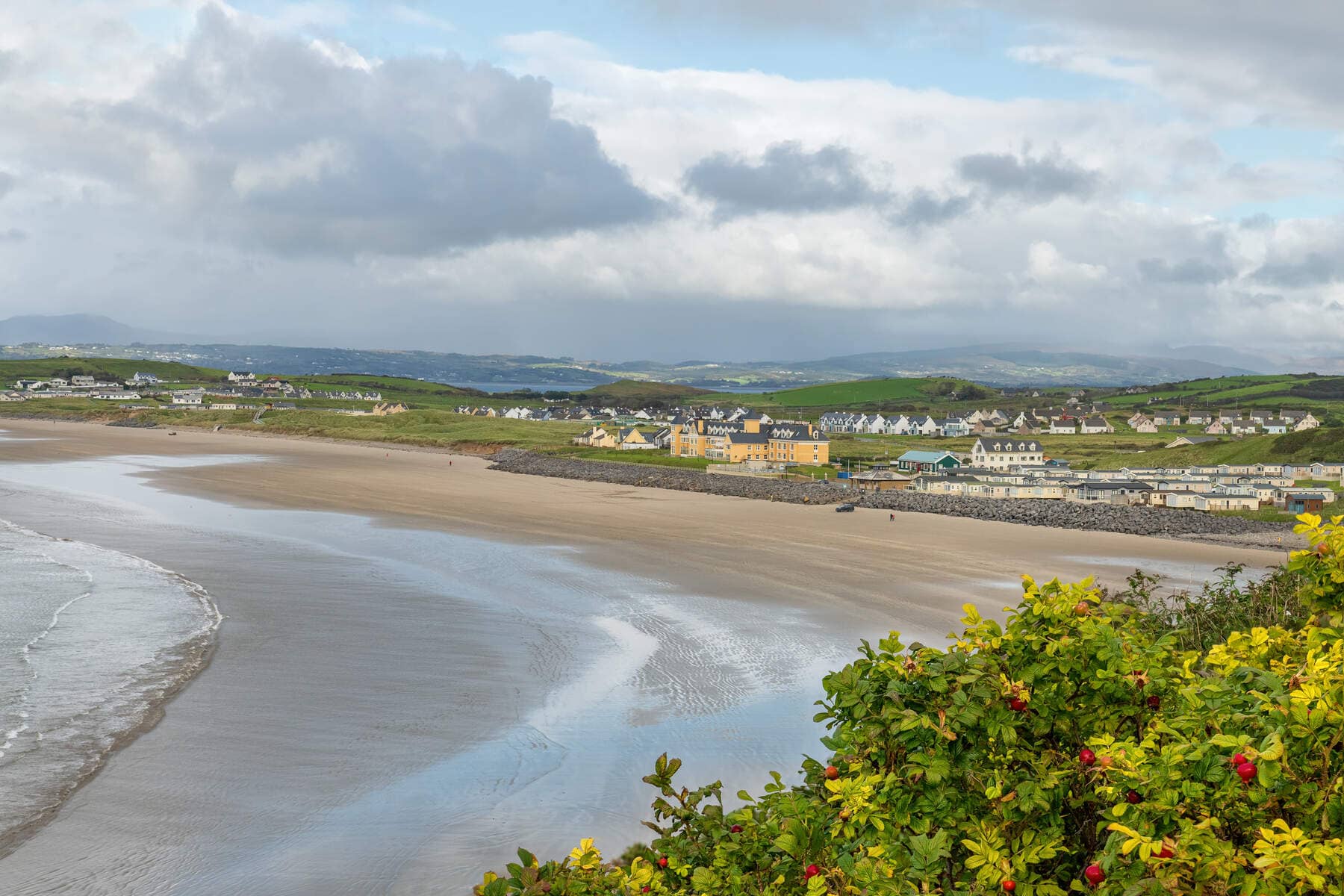 Wide view of Rossnowlagh Beach in County Donegal, with soft sands and coastal homes nestled in green hills.