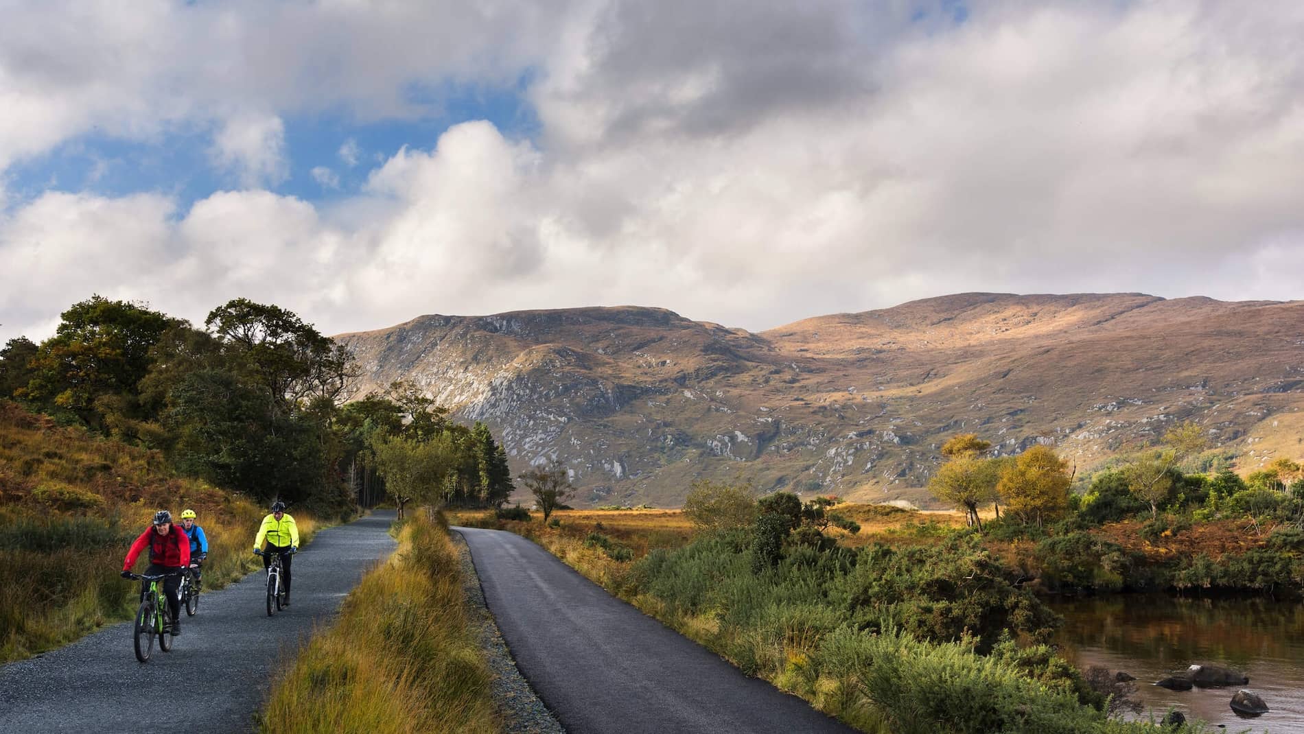 Group of cyclists on a trail through Glenveagh National Park with rugged mountains and autumn foliage, County Donegal.