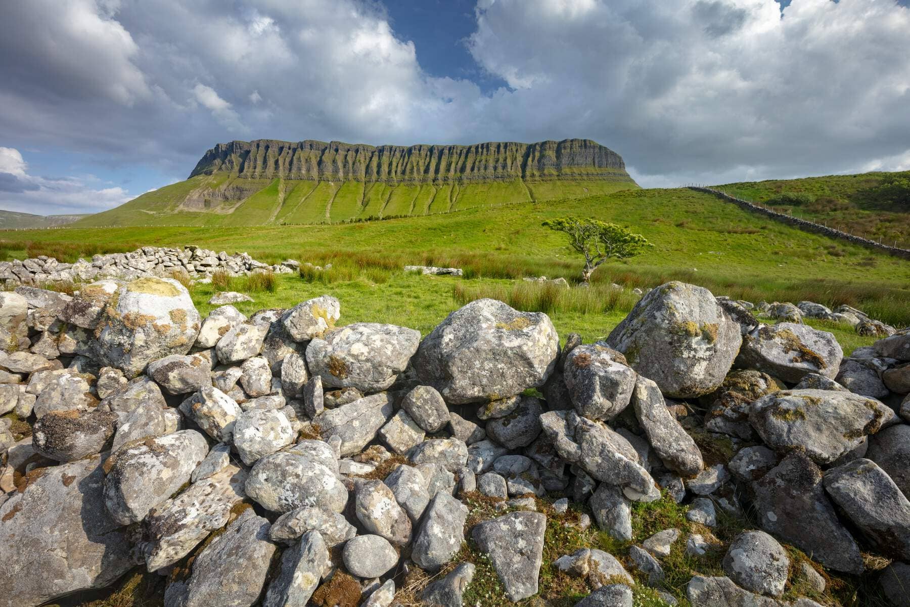 Ben Bulben mountain in County Sligo rising above green fields and a traditional dry stone wall under a dramatic sky.