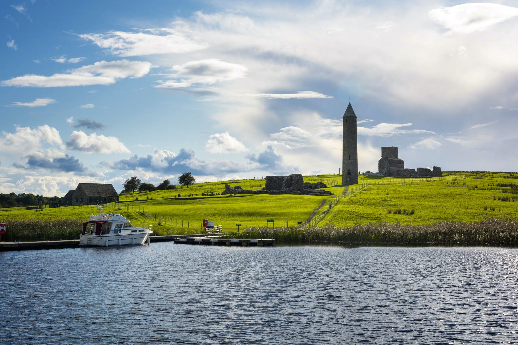 A boat docked at Devenish Island in County Fermanagh, with the ruins of a medieval round tower and church in the background.