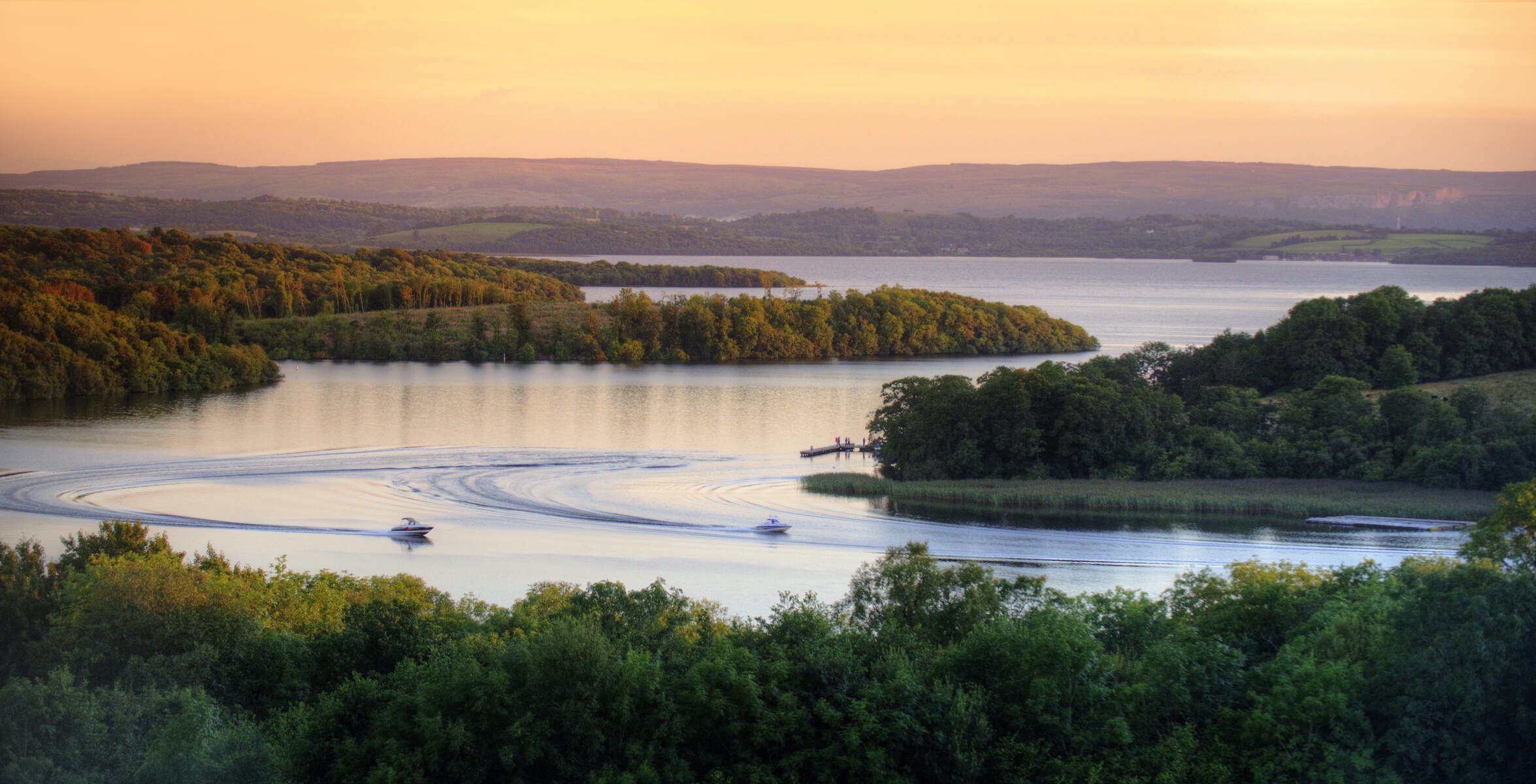 Two boats cruising through the tranquil Fermanagh Lakelands at sunset.