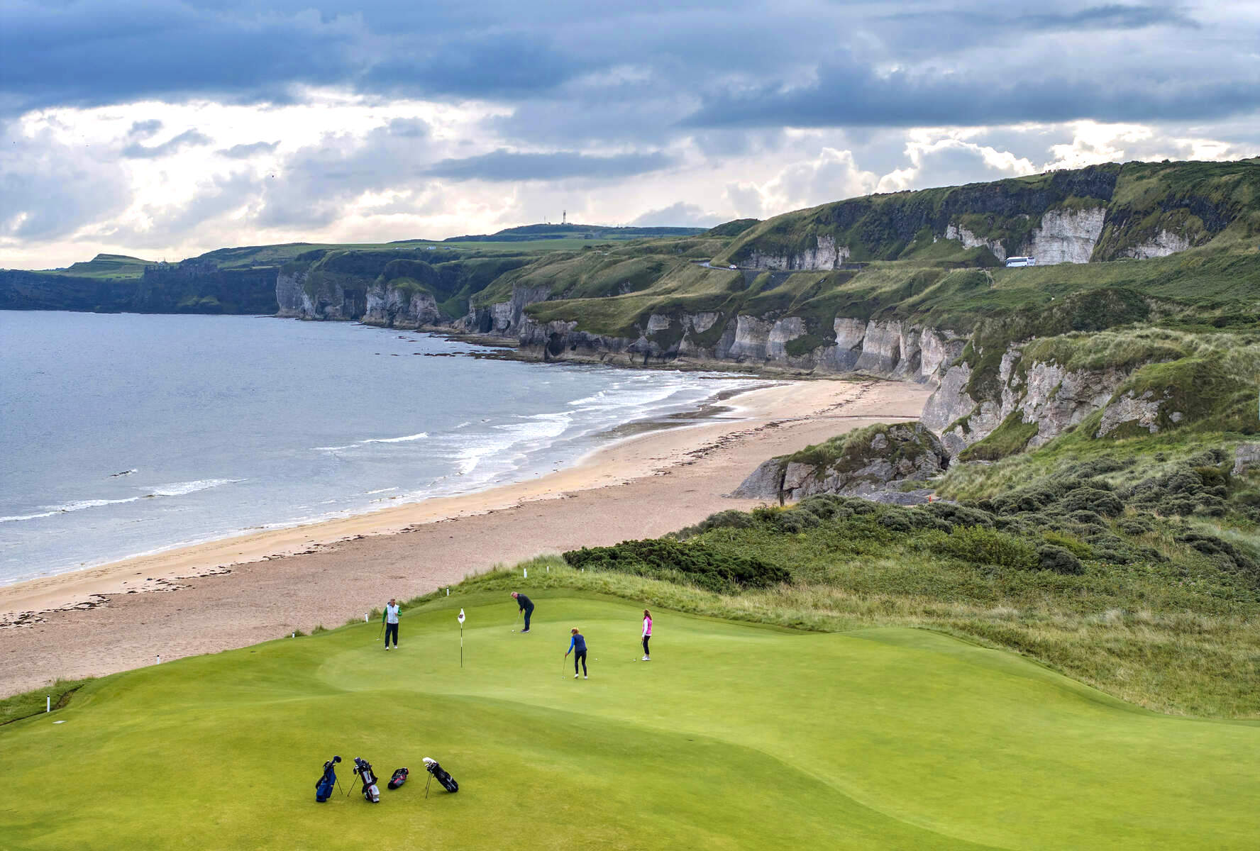 Golfers playing at Royal Portrush Golf Club with sea cliffs in the background.