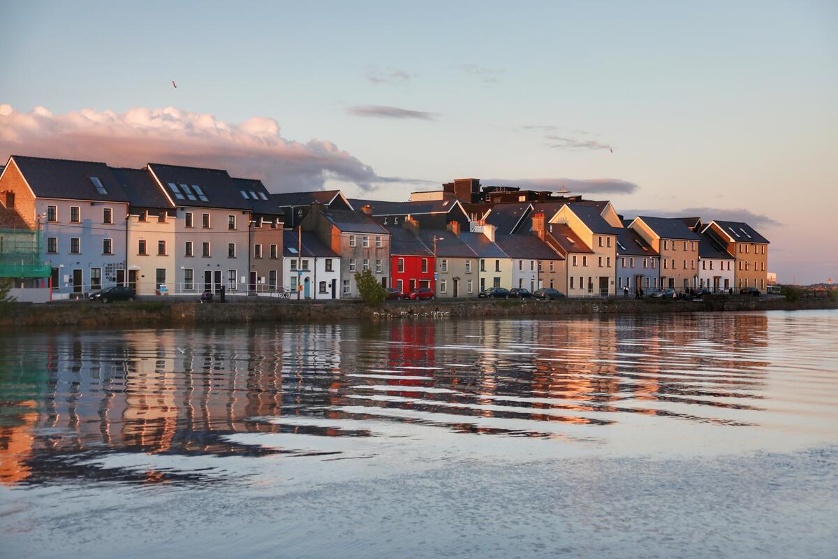 Colourful houses along The Claddagh reflected in the River Corrib at sunset in Galway City.