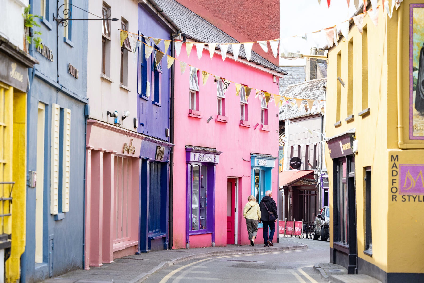 Couple walking down vibrant street in Kinsale, County Cork, with rainbow-coloured shopfronts.