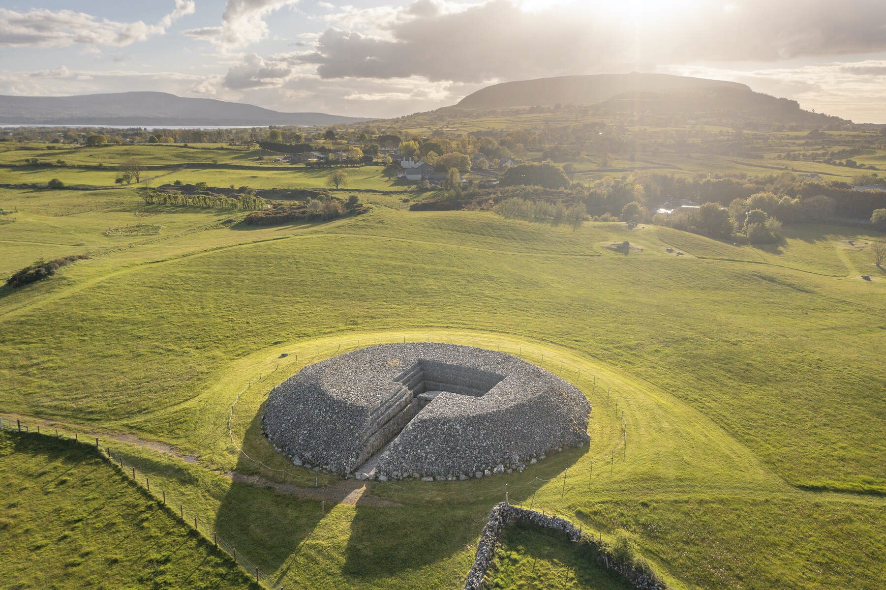 Stone cairn monument at Carrowmore Megalithic Cemetery set in rolling Sligo countryside with soft evening sunlight.
