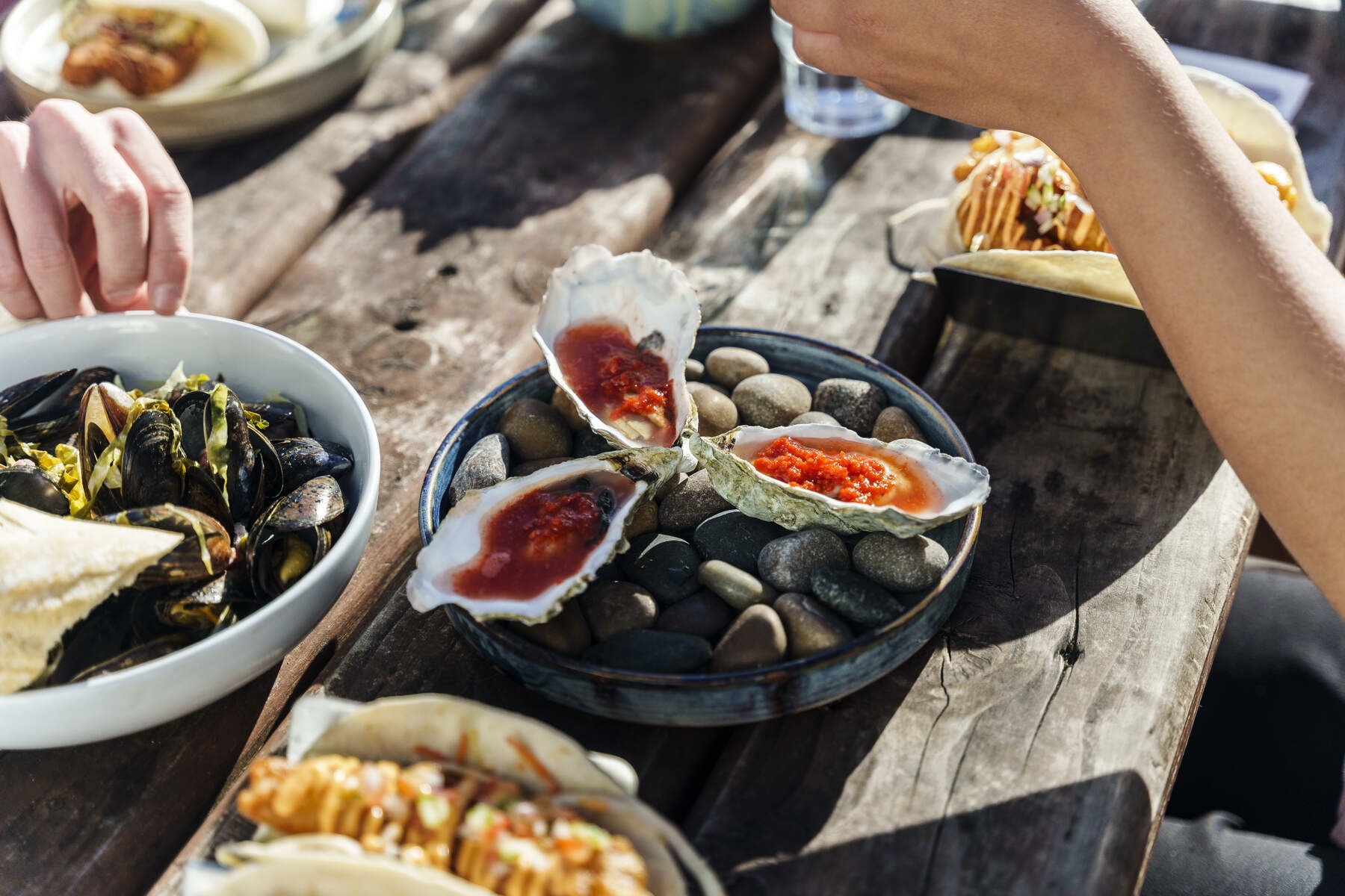 Fresh Irish oysters with red sauce served outdoors alongside mussels and tacos on a rustic table.