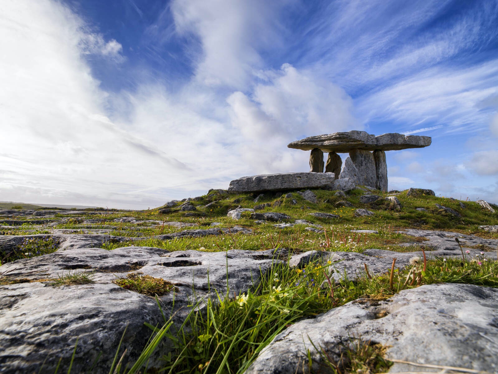 Poulnabrone dolmen standing on rocky limestone terrain of The Burren, County Clare, beneath a dramatic cloudy sky.