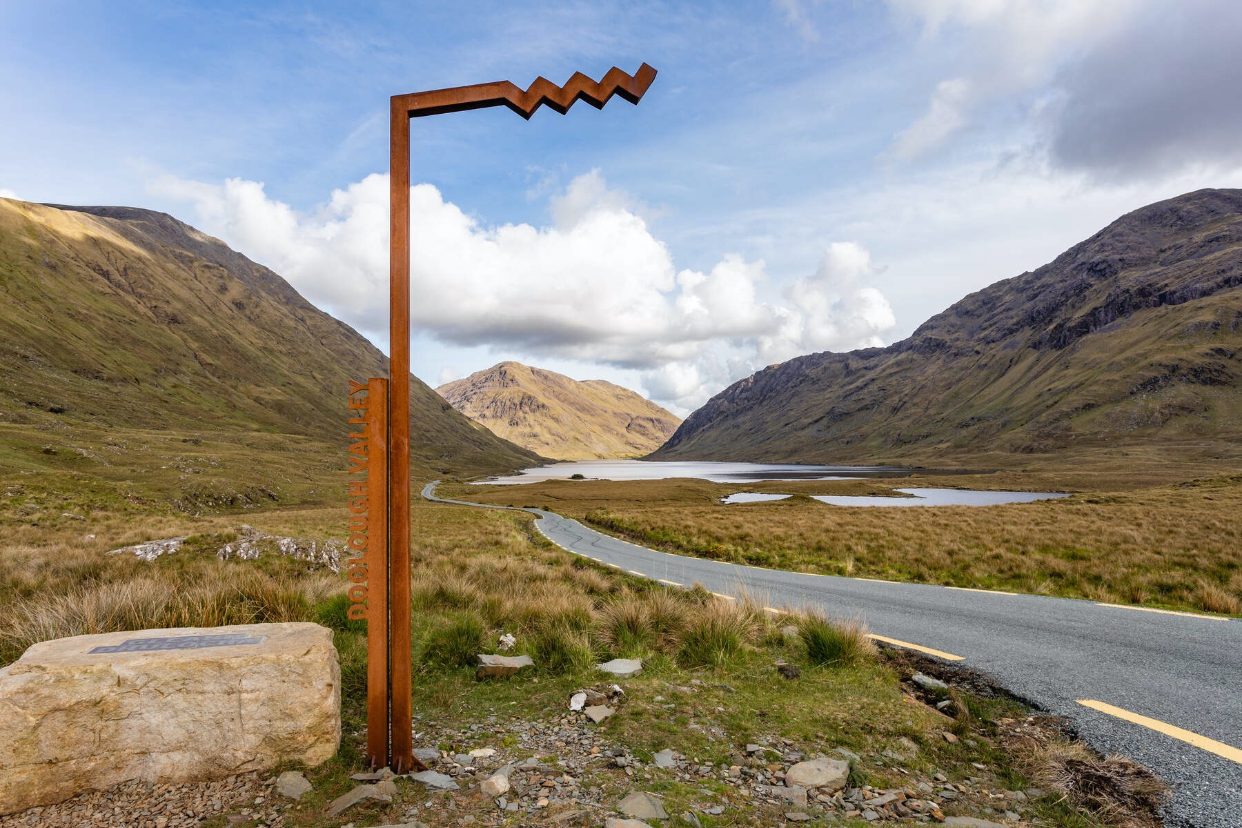 Scenic road curving through Mayo's rocky Doo Lough Valley with a Wild Atlantic Way marker sign.