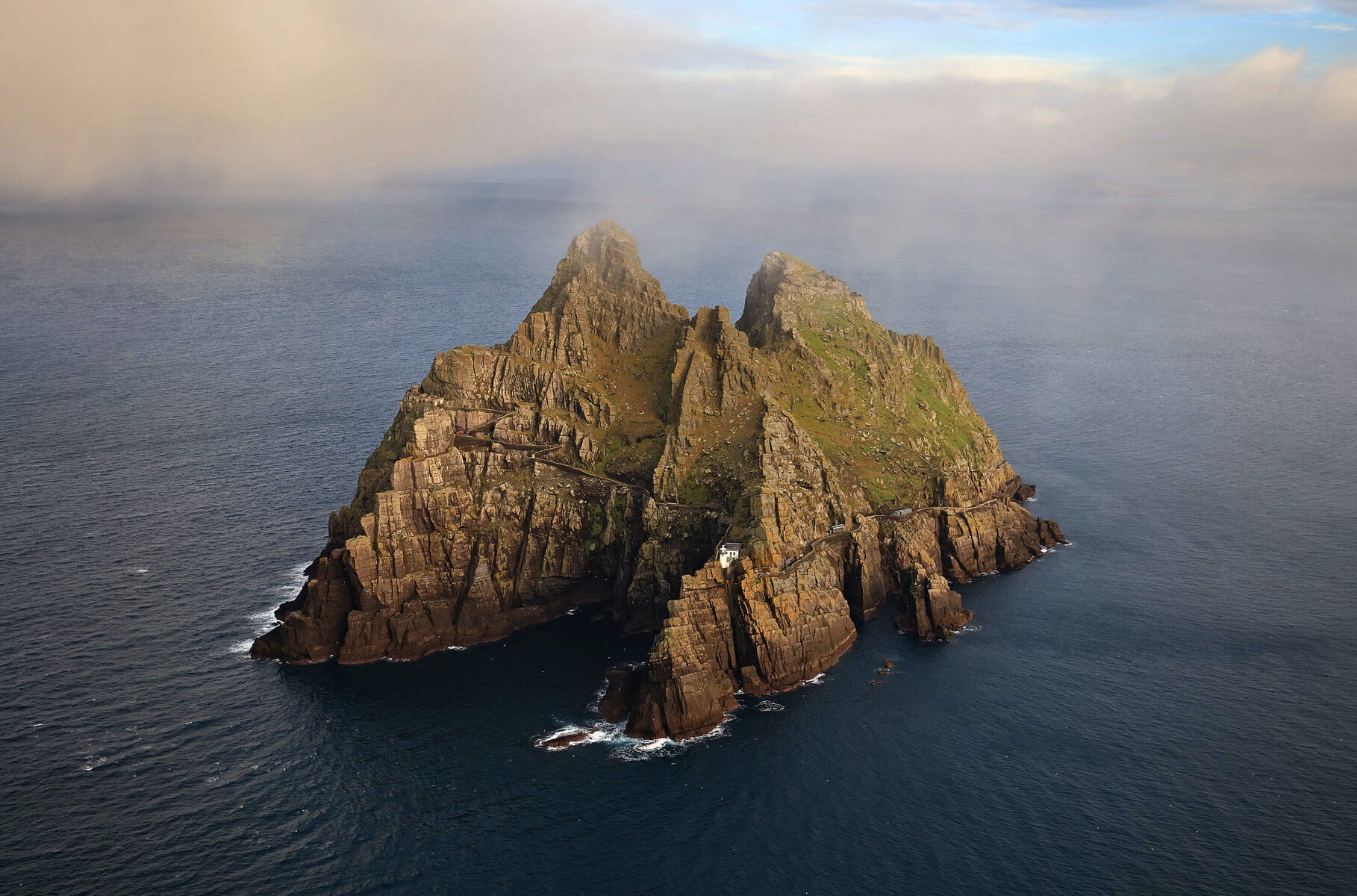 Steep rocky Skellig Michael island rising from sea under low cloud cover, off the Kerry coast.