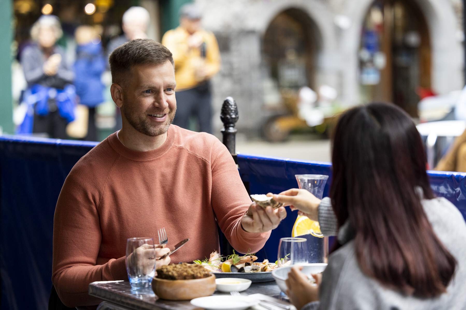 Man smiling at a woman while dining outdoors in Galway city with seafood and drinks on the table.