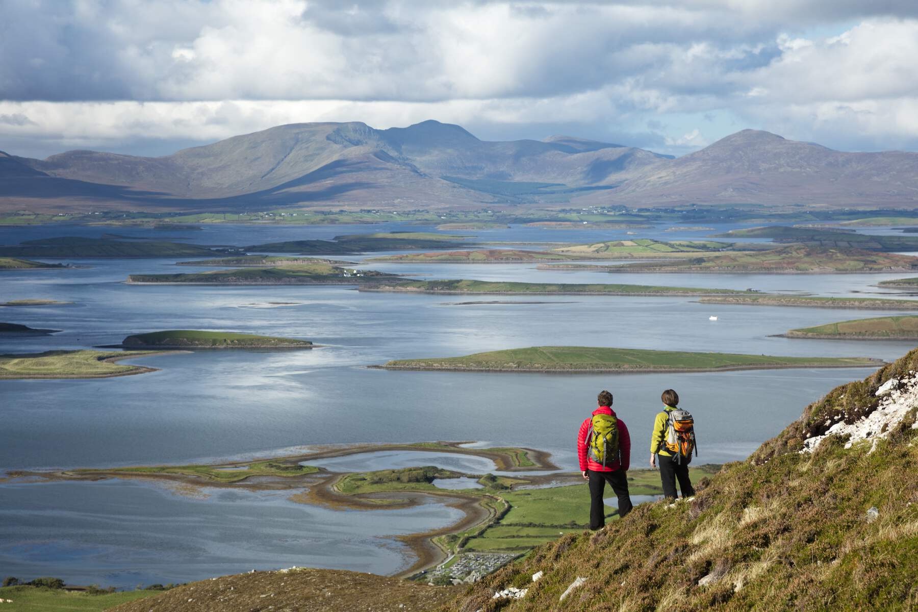 Two hikers overlooking Mayo's Clew Bay’s islands and calm waters from a hillside trail.