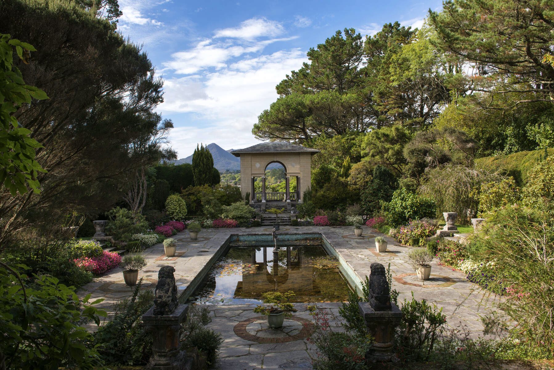 Ornamental pond garden with archway, flowers, and mountain backdrop at Garnish Island, County Cork.