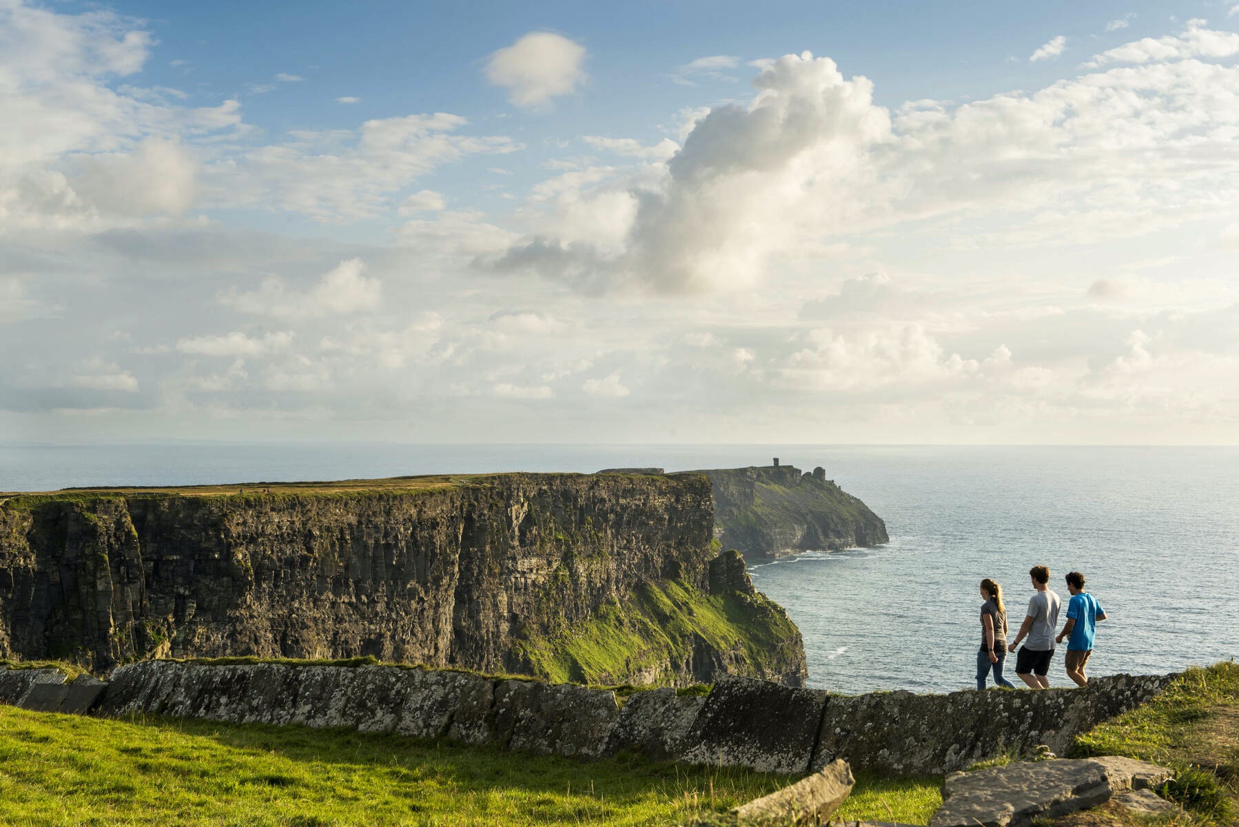 Group of people walking along the edge of the Cliffs of Moher in County Clare on a clear day.