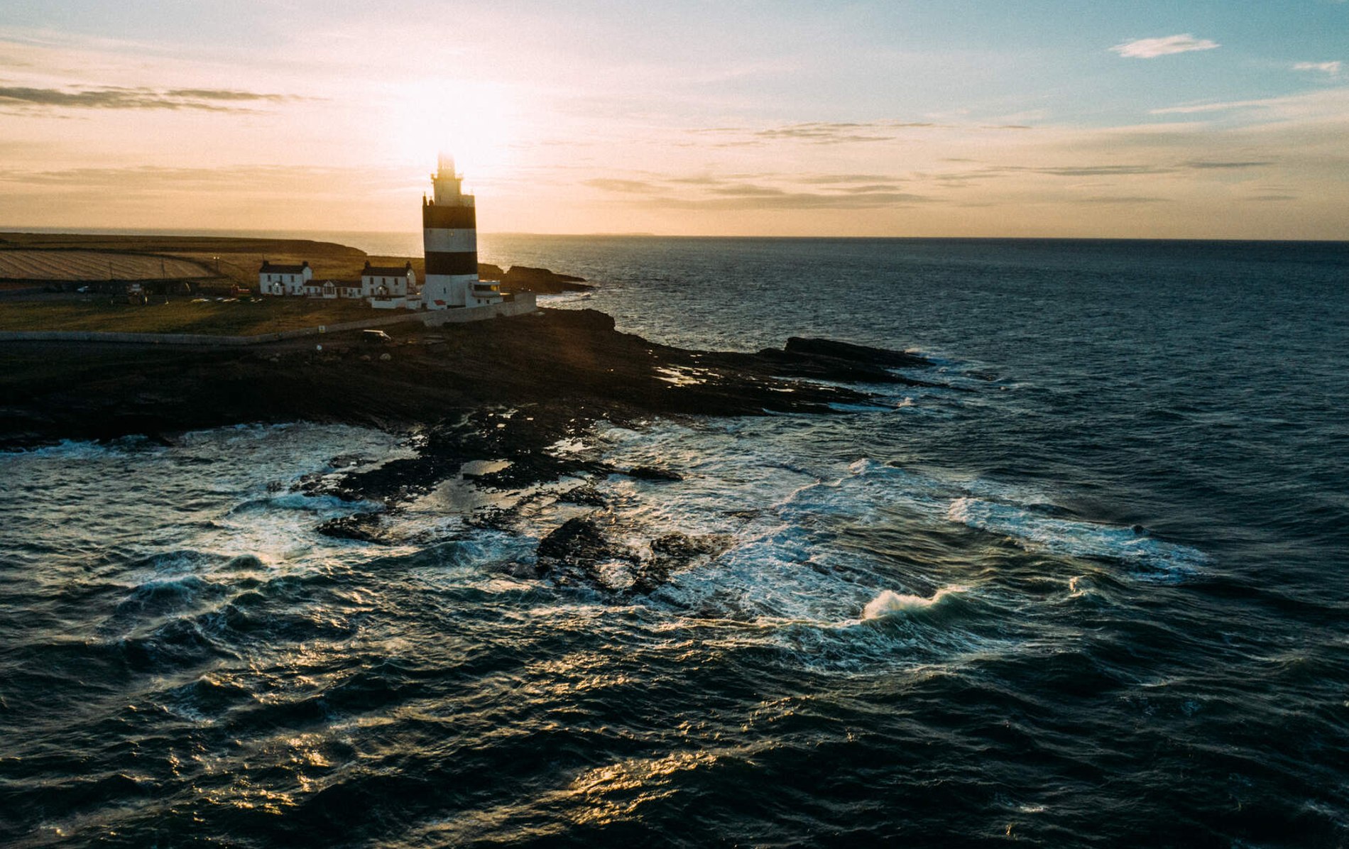 Sunset behind Hook Head Lighthouse in County Wexford, casting a warm glow over the rugged shoreline and Atlantic waves.