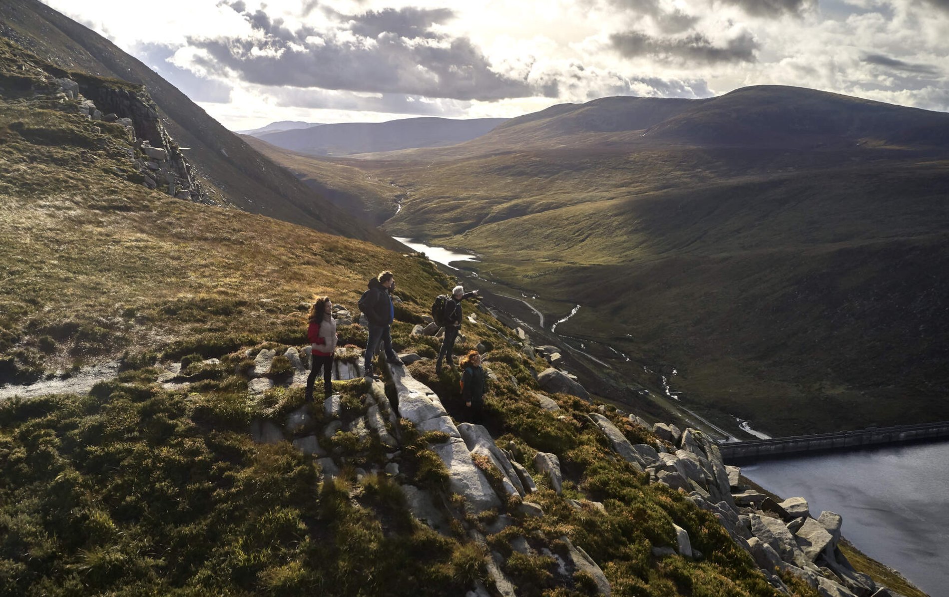 Hikers pausing on a ridge in the Mourne Mountains of County Down, taking in the panoramic view of valleys and distant peaks.