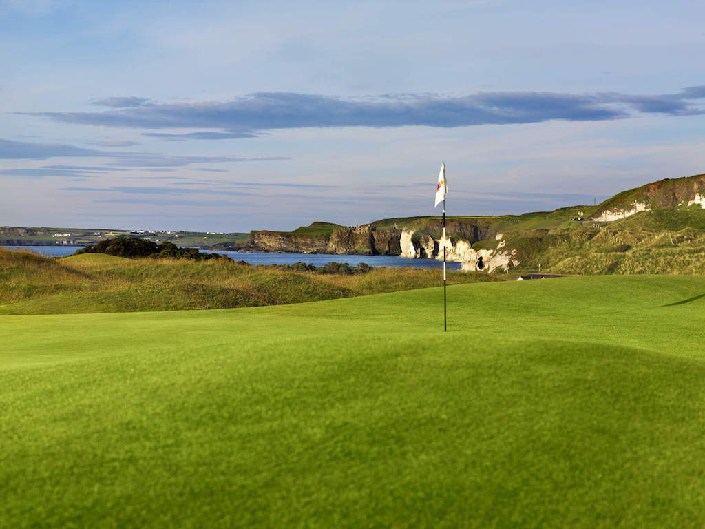 Flag on the green at Royal Portrush Golf Club overlooking cliffs and the Atlantic Ocean.