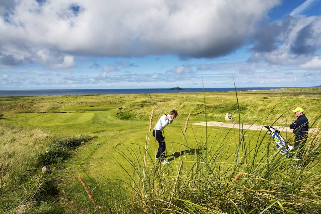 Golfer preparing to swing at Ballyliffin Golf Course with Atlantic Ocean views beyond the dunes.