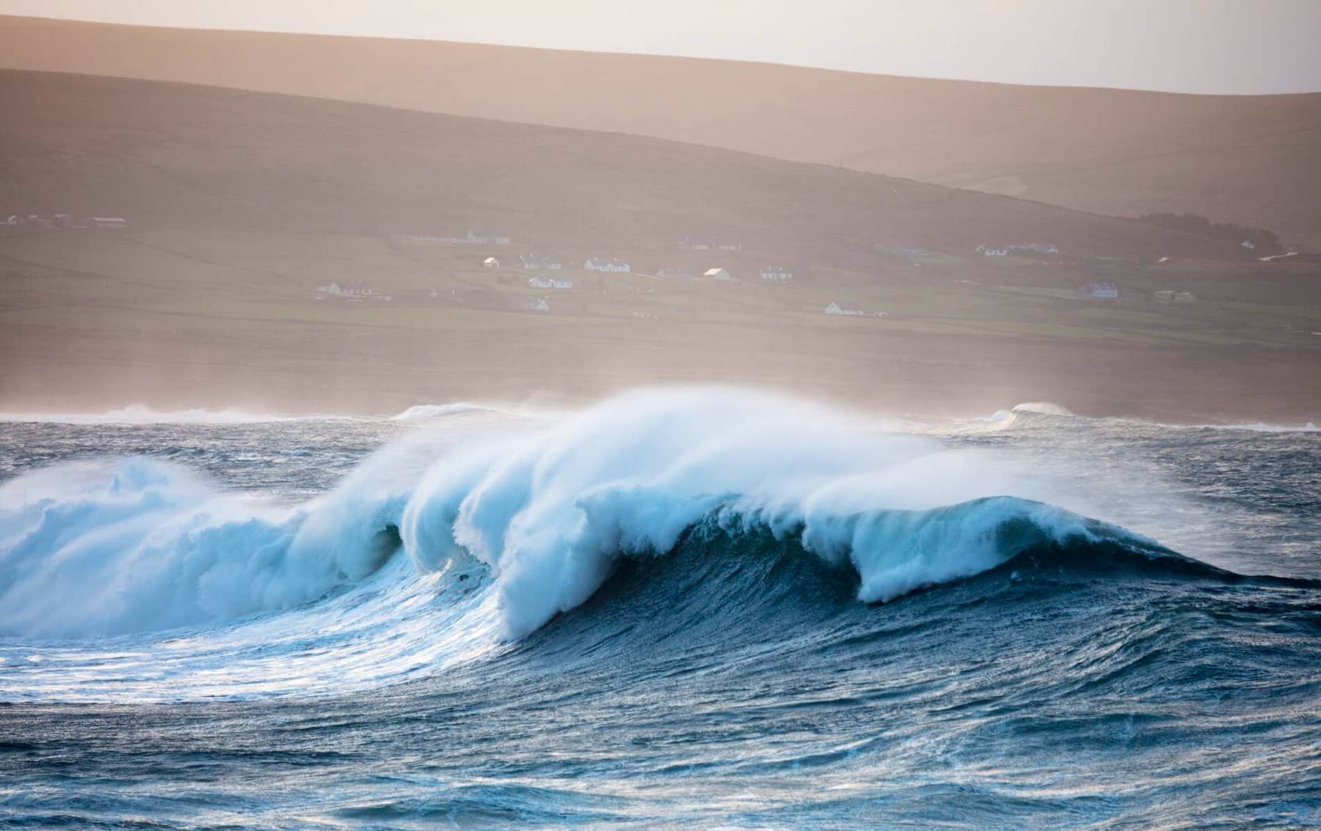Large ocean wave rolls toward shore beneath pink sky in Ireland, illustrating scuba diving adventure theme.