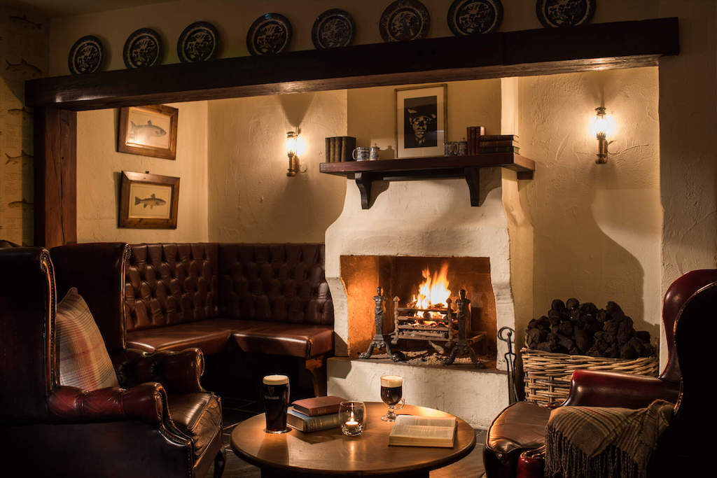 Traditional pub snug with leather seating, books and drinks by the fireplace at Bushmills Inn, County Antrim.