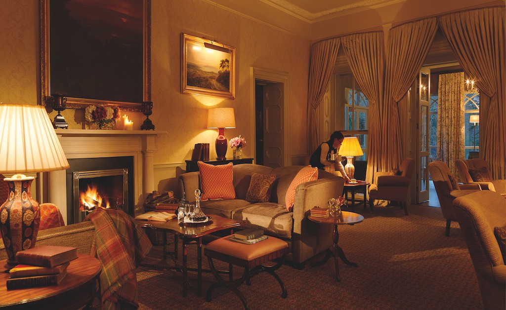 Luxurious lounge with a glowing fire, plush sofas and warm ambient lighting at Ballynahinch Castle Hotel, County Galway.