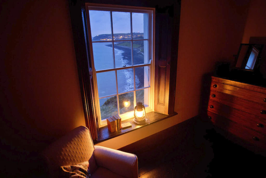 Cosy room with a lantern-lit window overlooking the Irish coastline at Blackhead Lightkeeper’s House, County Antrim.