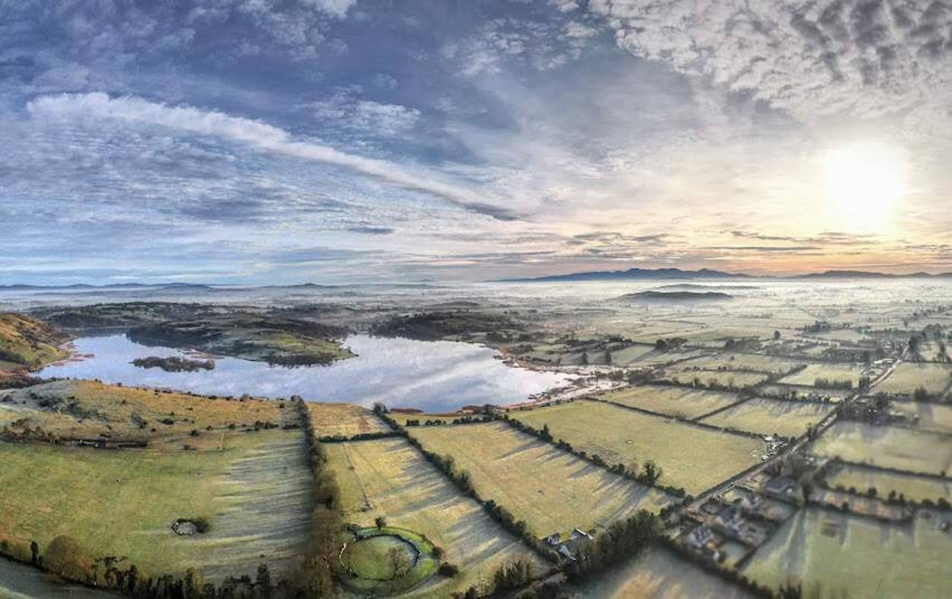 Lough Gur glistens in the soft light of winter with frosted fields and distant hills.