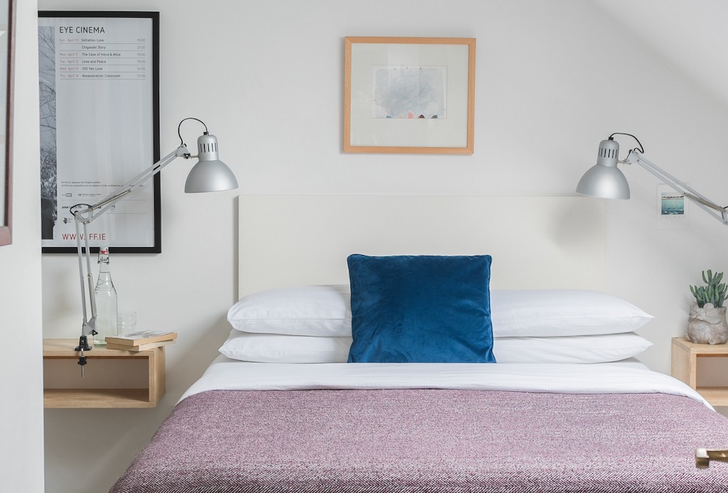 Bright guest bedroom at The Stop B&B in Galway with double bed, blue cushion and reading lamps on white walls.