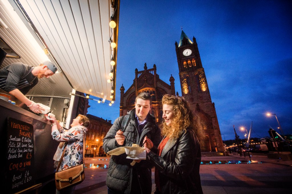 Street food stall at night in Derry~Londonderry with people enjoying takeaway outside the Guildhall.