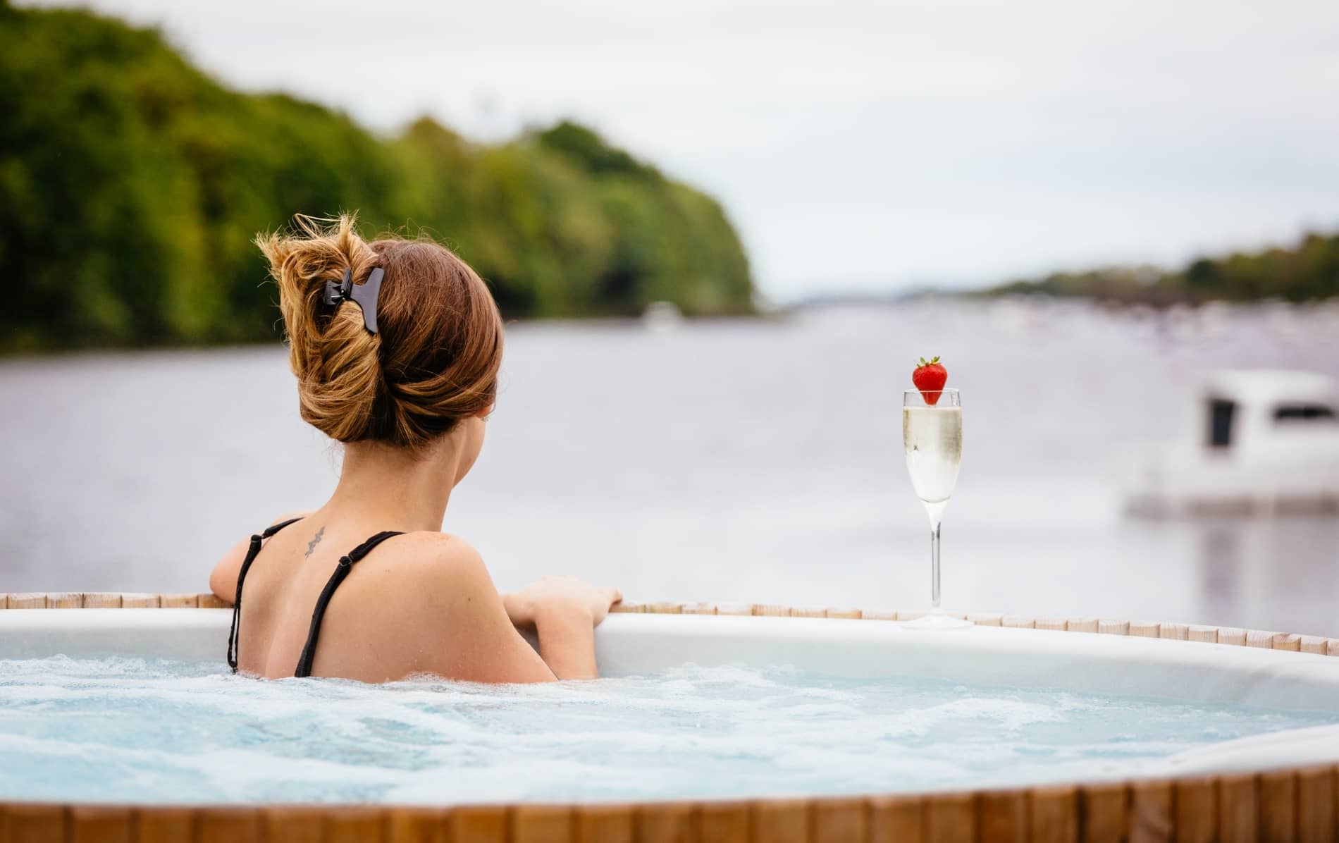 Woman relaxing in a hot tub by a lake with a glass of champagne in Ireland.