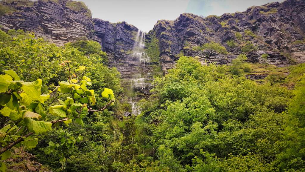 The Devil's Chimney cascades down a rugged cliff surrounded by lush trees and greenery in County Leitrim.